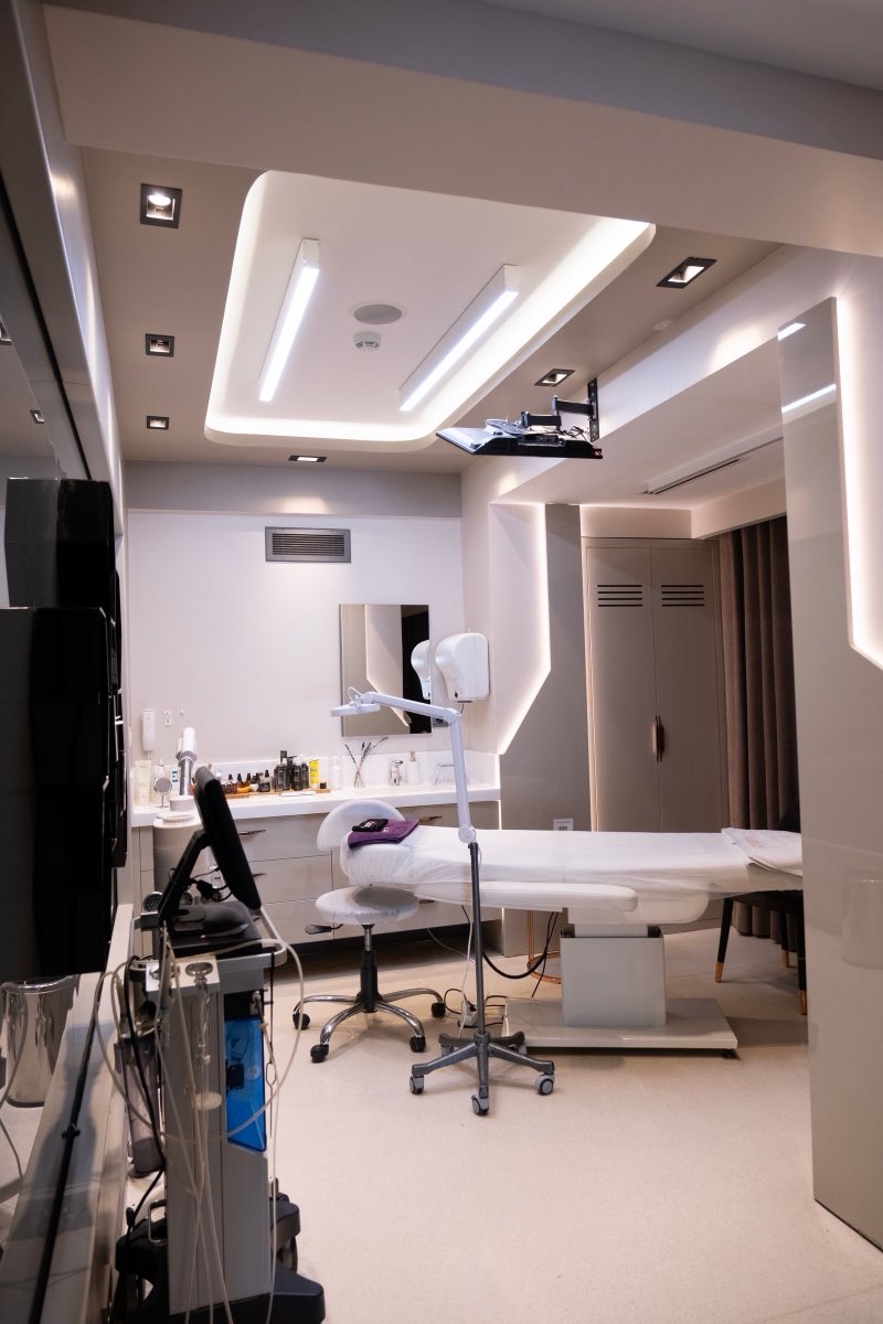A treatment room with a couch under a recessed lit ceiling, a device on a wheeled stand beside it and a second machine against the wall.