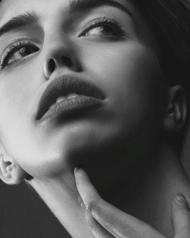 Black and white studio close up of a woman looking upward, her chin resting on her fingers.
